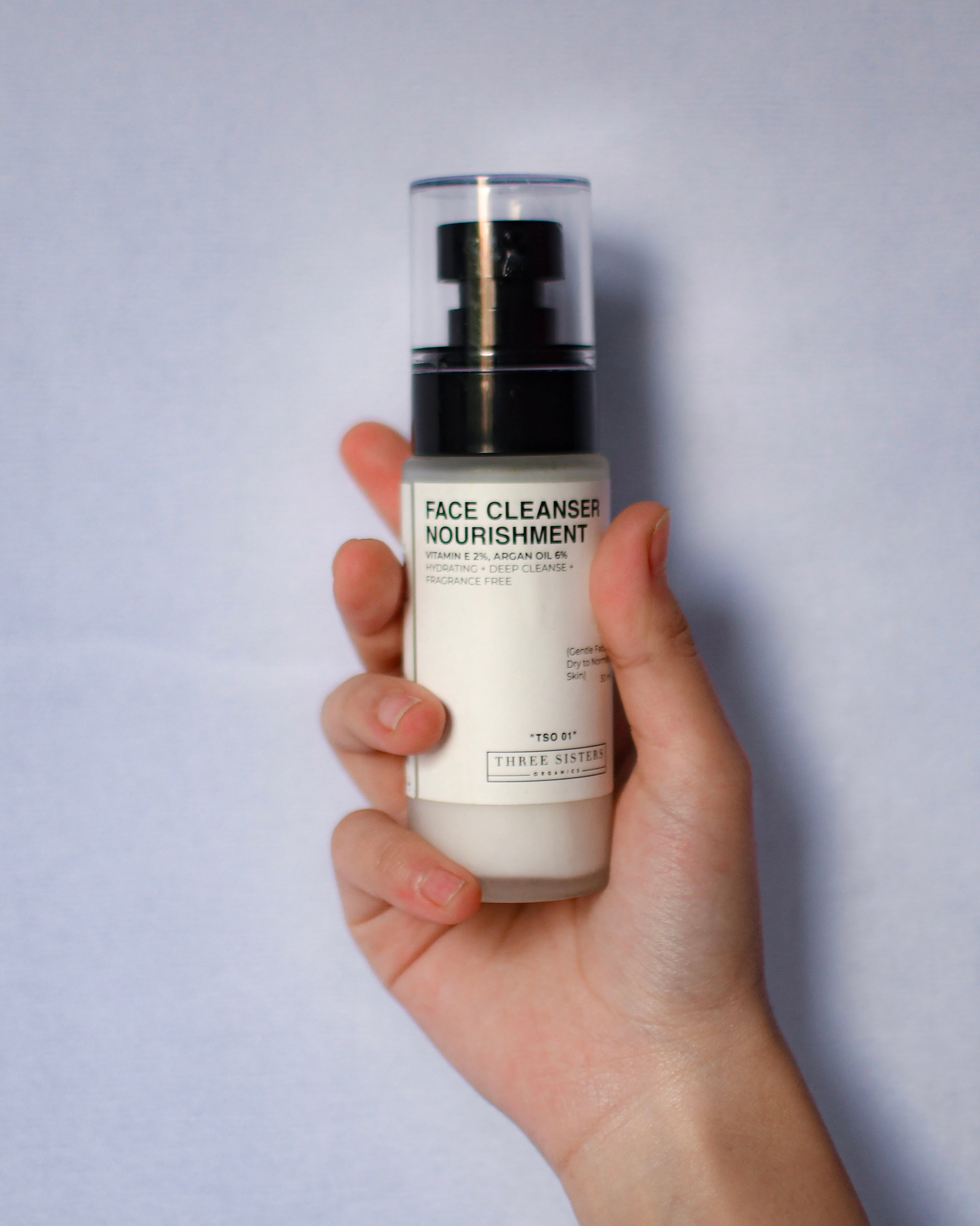 Face Cleanser Nourishment, Gentle Face Cleanser for all skin types, hand holding the glass bottle with black pump, front view