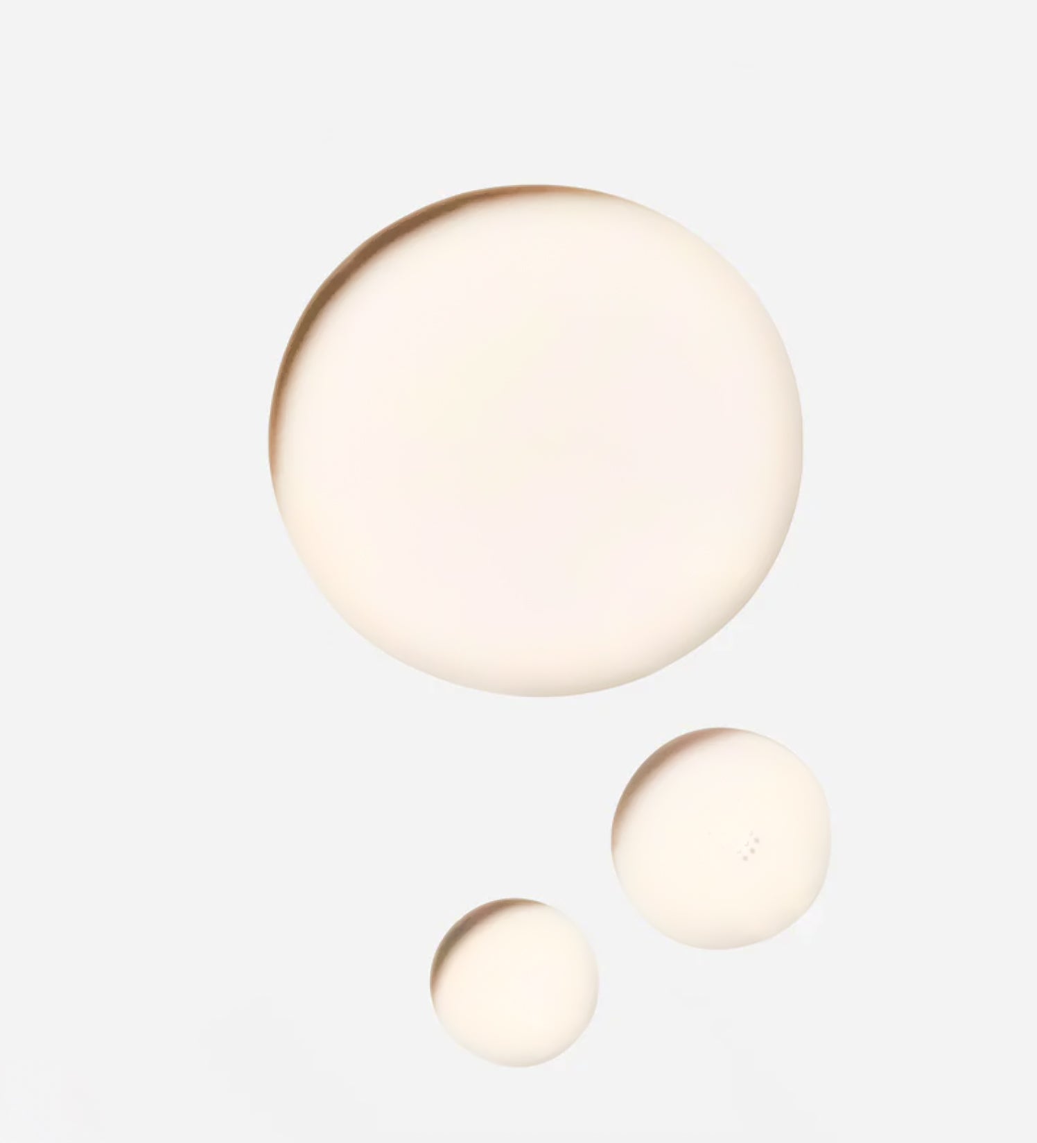 Three spherical droplets of pregnancy oil of varying sizes on a light grey background