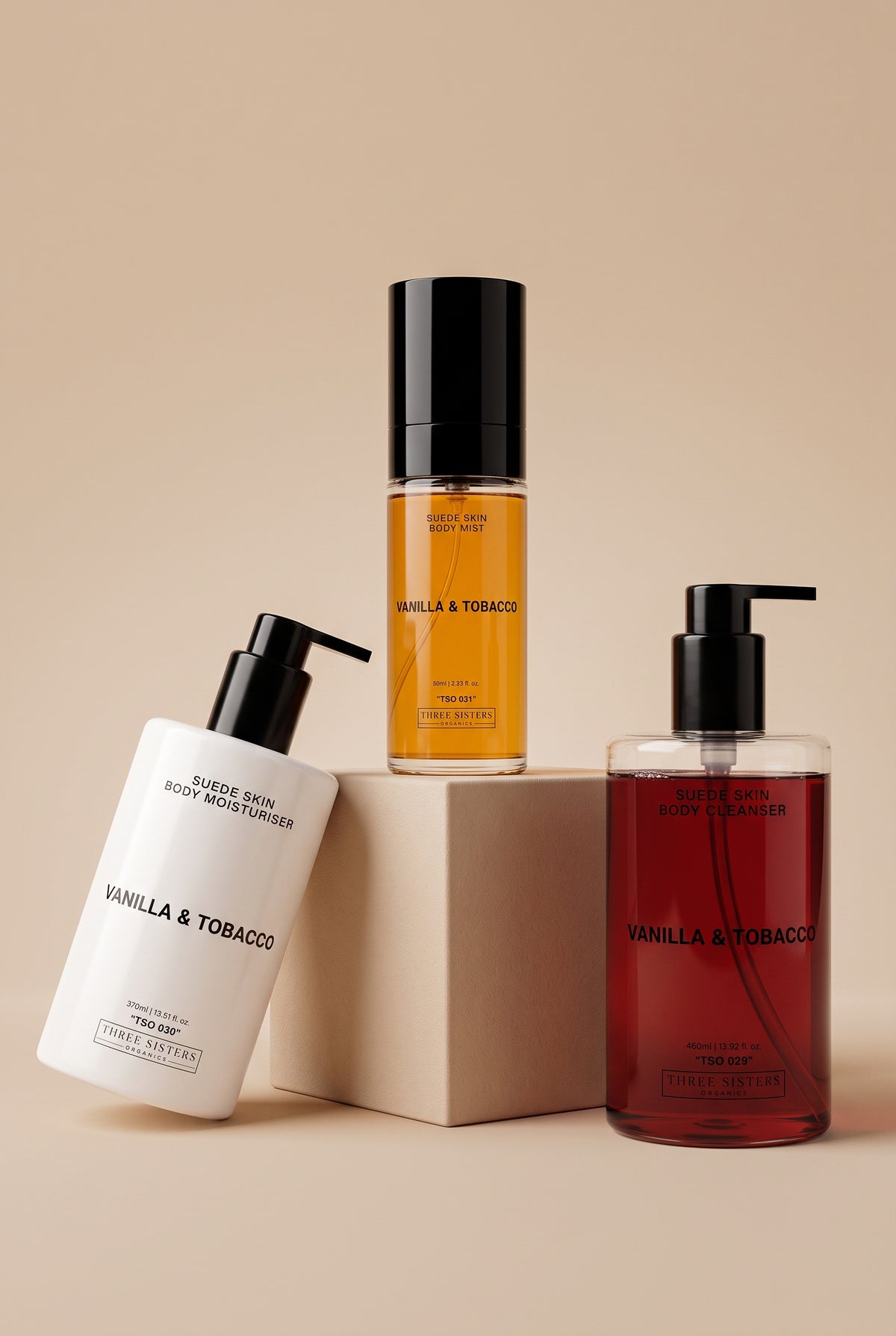 Three bottles of Vanilla & Tobacco Body Wash , Mist and Cream on a soft beige background