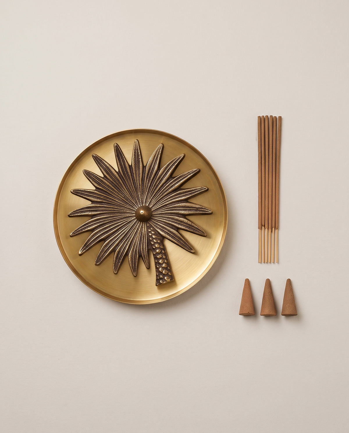 brass incense stand holder in the shape of a palm tree placed on a brass plate with 6 incense sticks and 3 dhoop cones on a ivory beige background