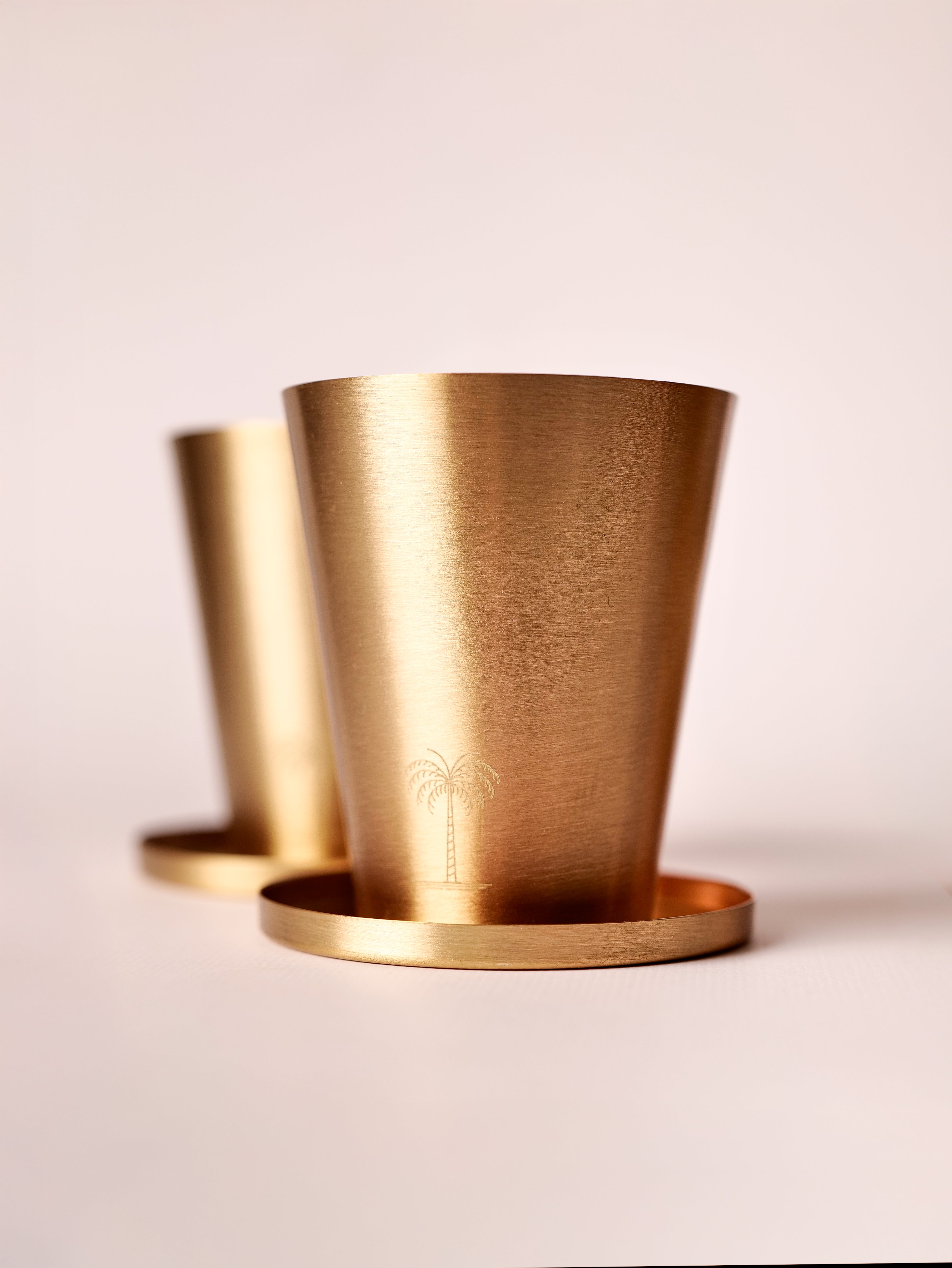 Close up of a brass tumbler with coaster. tumbler has a small palm tree motif