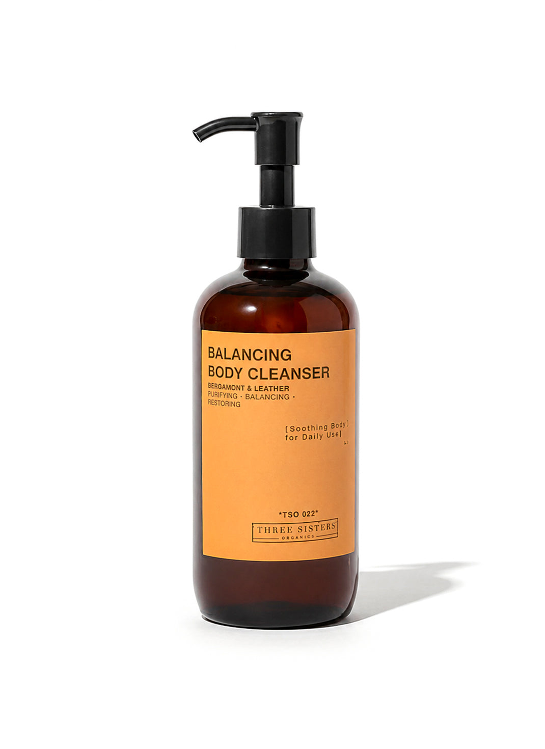 A bottle of Three Sisters Organics Balancing Body Cleanser with an amber plastic body, black pump dispenser, and a bright orange label, set against a plain white background.