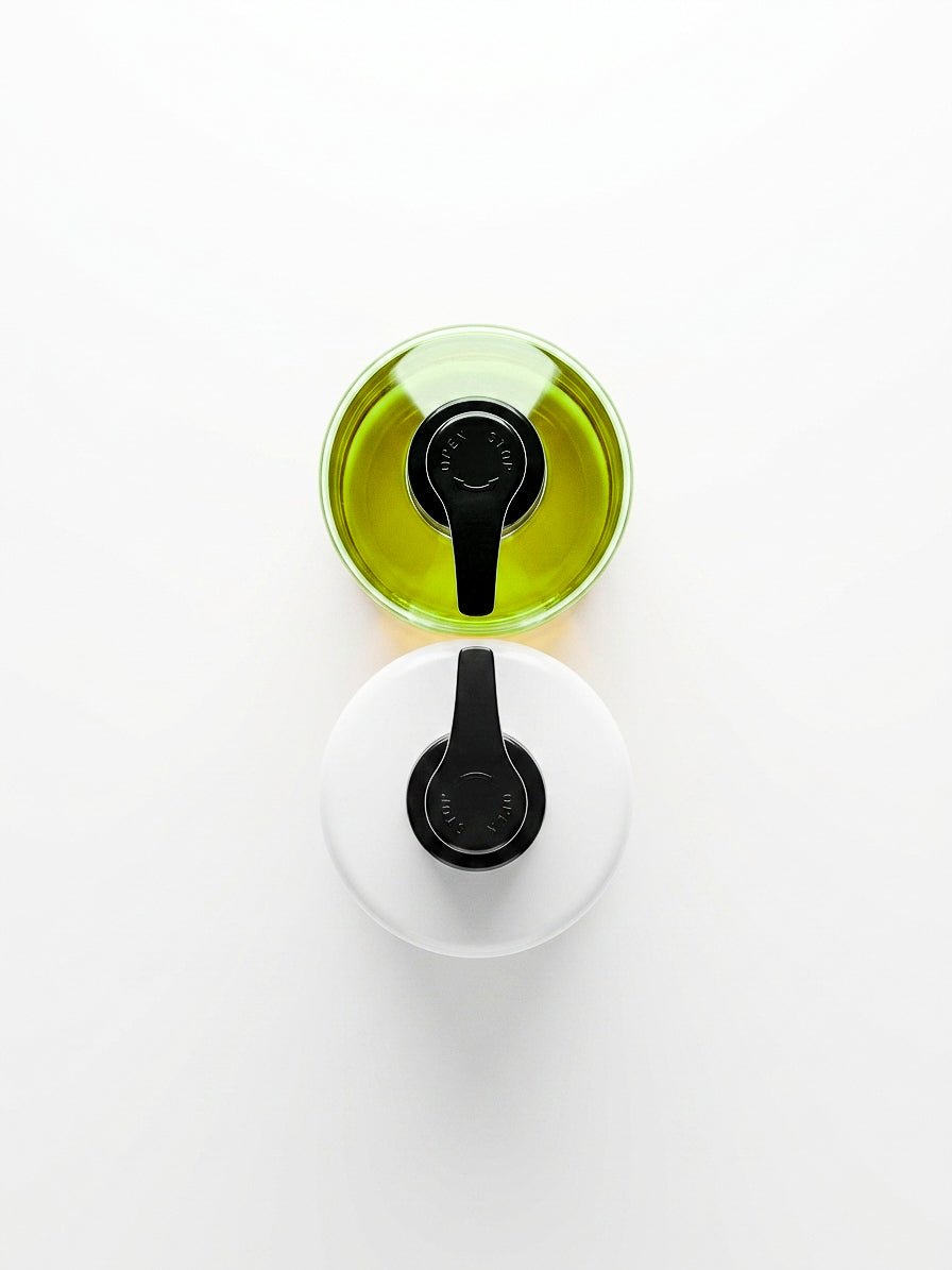 Two round hand care bottles with black pour spouts, one filled with green hand wash and one with hand lotion in white, arranged vertically on a clean white background.