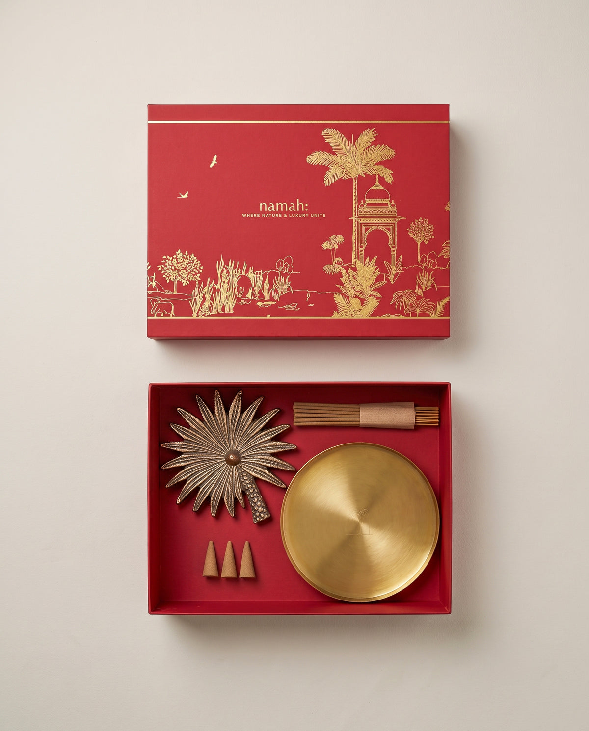 brass incense stand holder  in the shape of a palm tree placed and a brass plate with 6 incense sticks and 3 dhoop cones placed in a red luxury gift box on a ivory beige background
